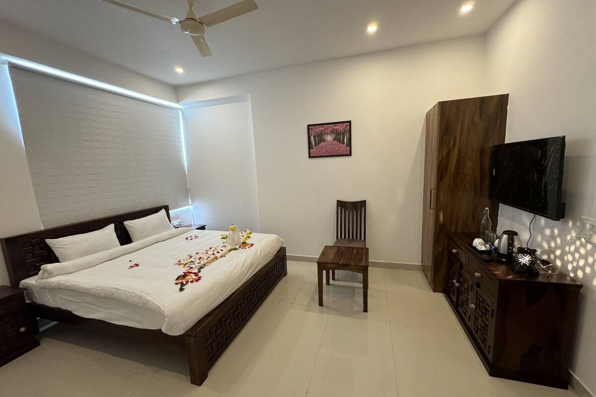 A hotel room with a bed, a chair, a TV, and a wooden wardrobe.