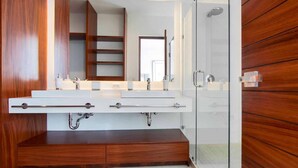 Ein modernes Badezimmer mit einem Holzbadezimmermöbel, einem großen Spiegel und einer Duschkabine aus Glas.