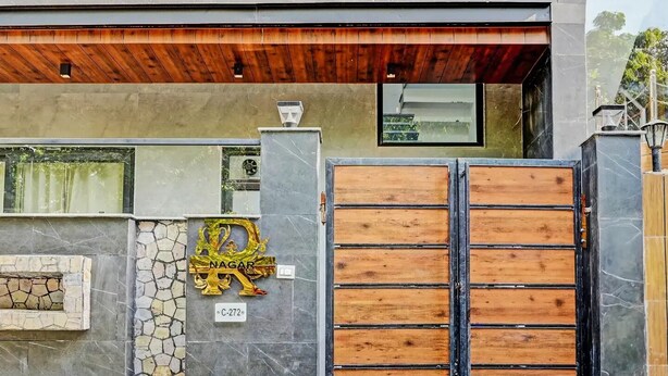 A modern house with a large wooden gate, a stone wall with a decorative sign, and a tiled entrance. - Kashvi Residency (Greater Noida)