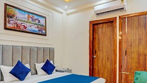 A bedroom with a large bed, a wooden wardrobe, and a painting on the wall. - Kashvi Residency (Greater Noida)