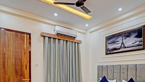 A modern bedroom with a large bed, a wooden door, a ceiling fan, and a framed picture of the Eiffel Tower. - Kashvi Residency (Greater Noida)