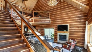 Ein geräumiger Holzblockbau mit Treppe, Kamin und gemütlichem Sitzbereich.