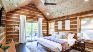 Ein Schlafzimmer einer Holzhütte mit Bett, Nachttisch, Lampe und Blick ins Freie.
