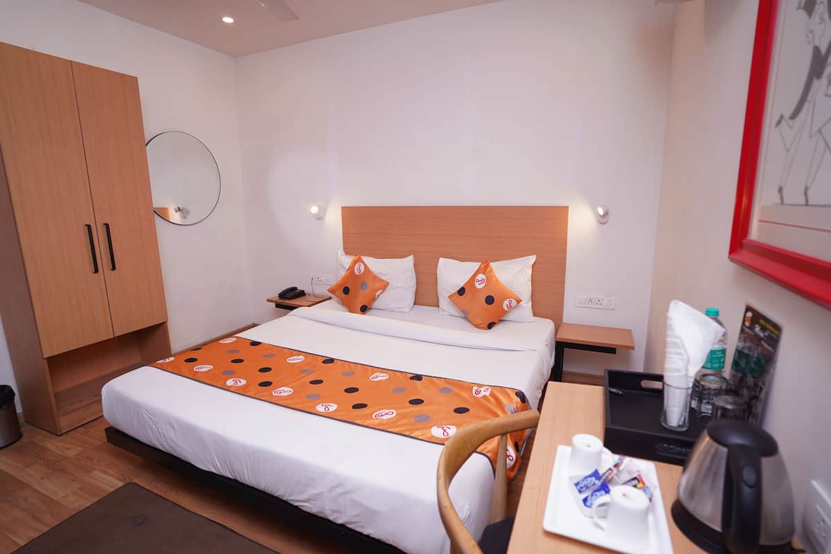 Ein Hotelzimmer mit einem Bett, einem Schreibtisch mit Wasserkocher, einem Stuhl, einem Kleiderschrank und einem Spiegel an der Wand.