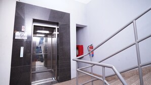 Un ascensor amb una porta de vidre, un extintor fixat a la paret i una barana metàl·lica.