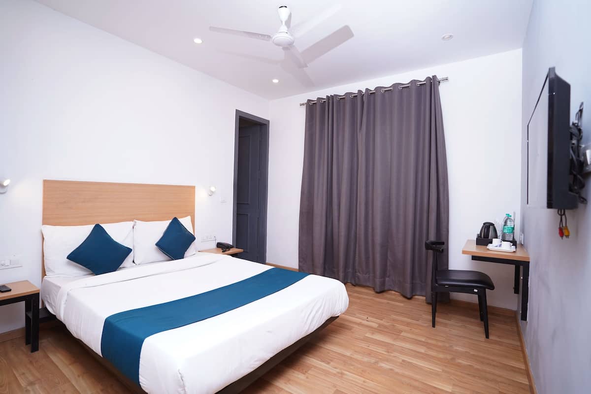 Ein Hotelzimmer mit Bett, Schreibtisch, Stuhl, Deckenventilator und Vorhang.
