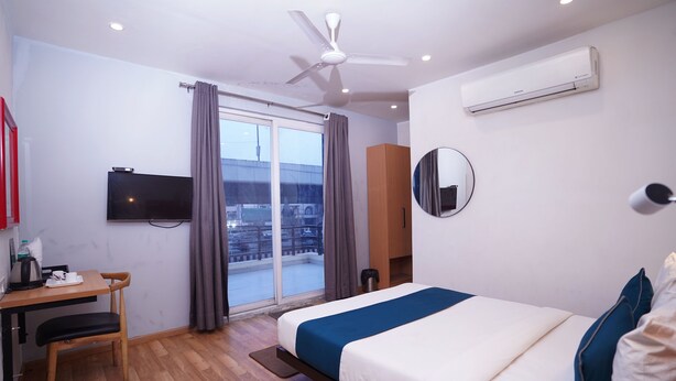 Una habitació d'hotel moderna amb un llit, un escriptori amb una cadira, una televisió i una finestra gran amb cortines.