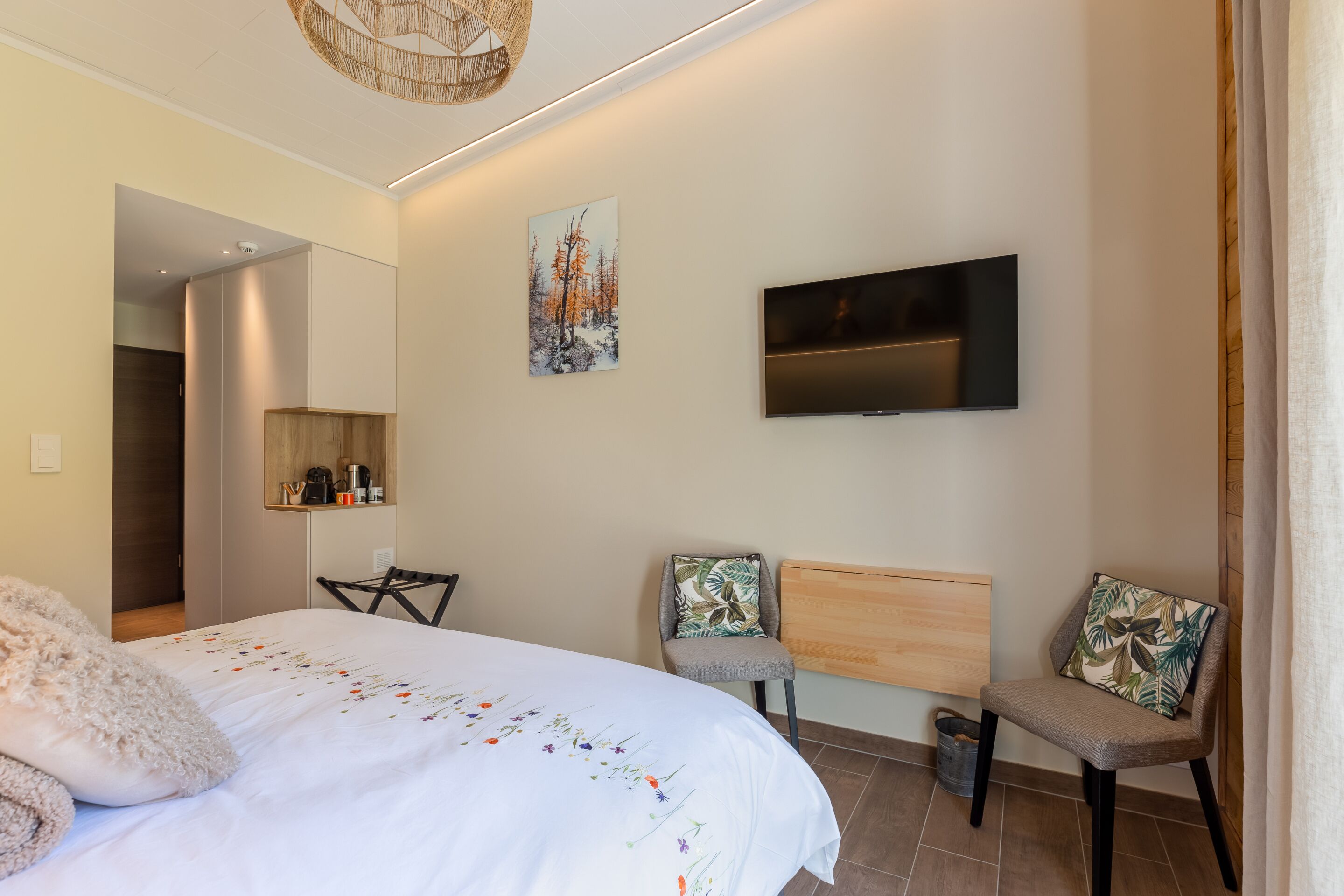 Camera da letto moderna con un letto, due sedie, una TV e un quadro appeso al muro.