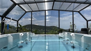 Un espace abrité, avec un jacuzzi, entièrement vitré et offrant une vue dégagée sur le paysage environnant.