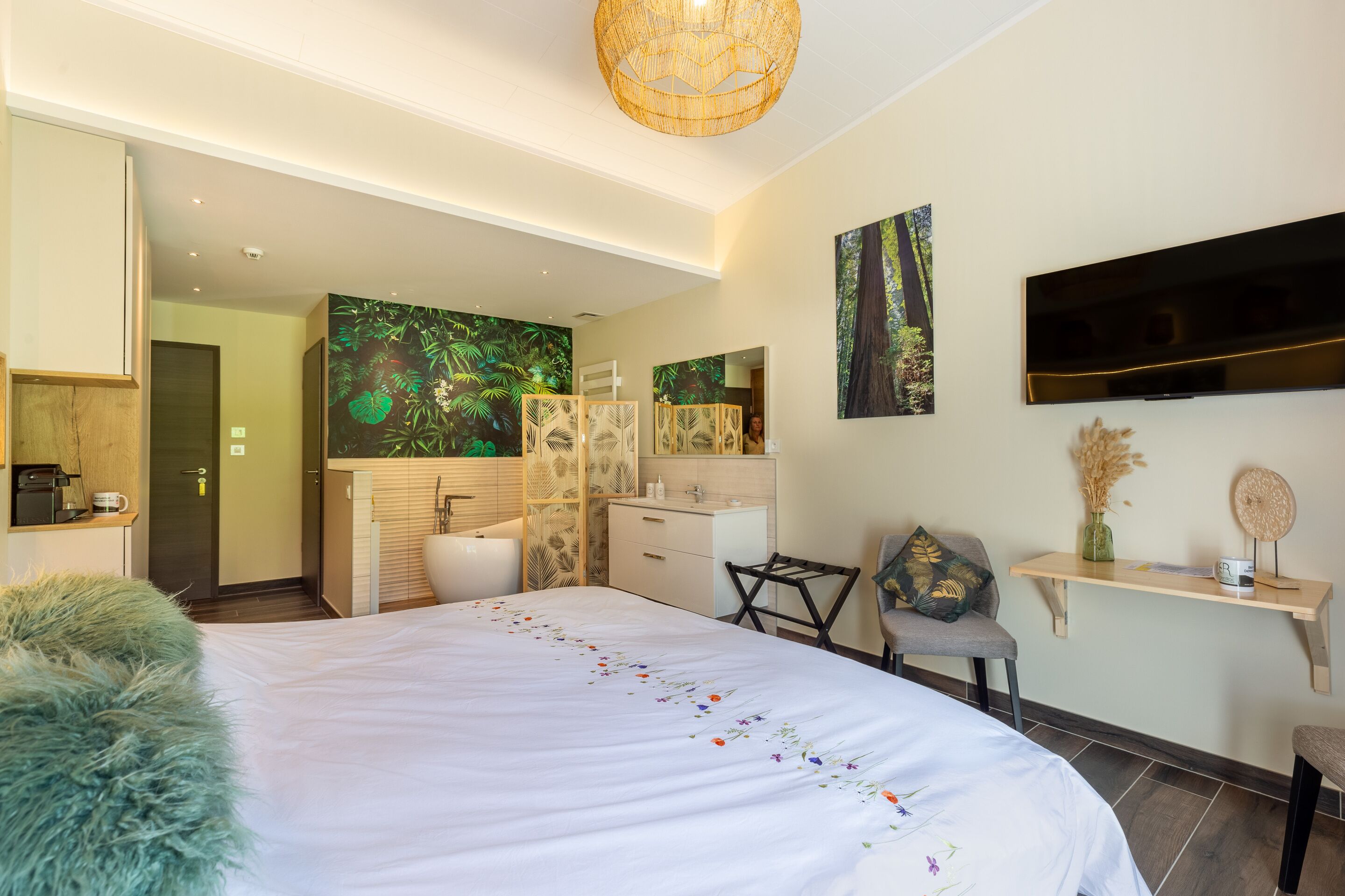 Habitación de hotel moderna con una cama grande, televisor, escritorio y baño visible a través de una puerta abierta.