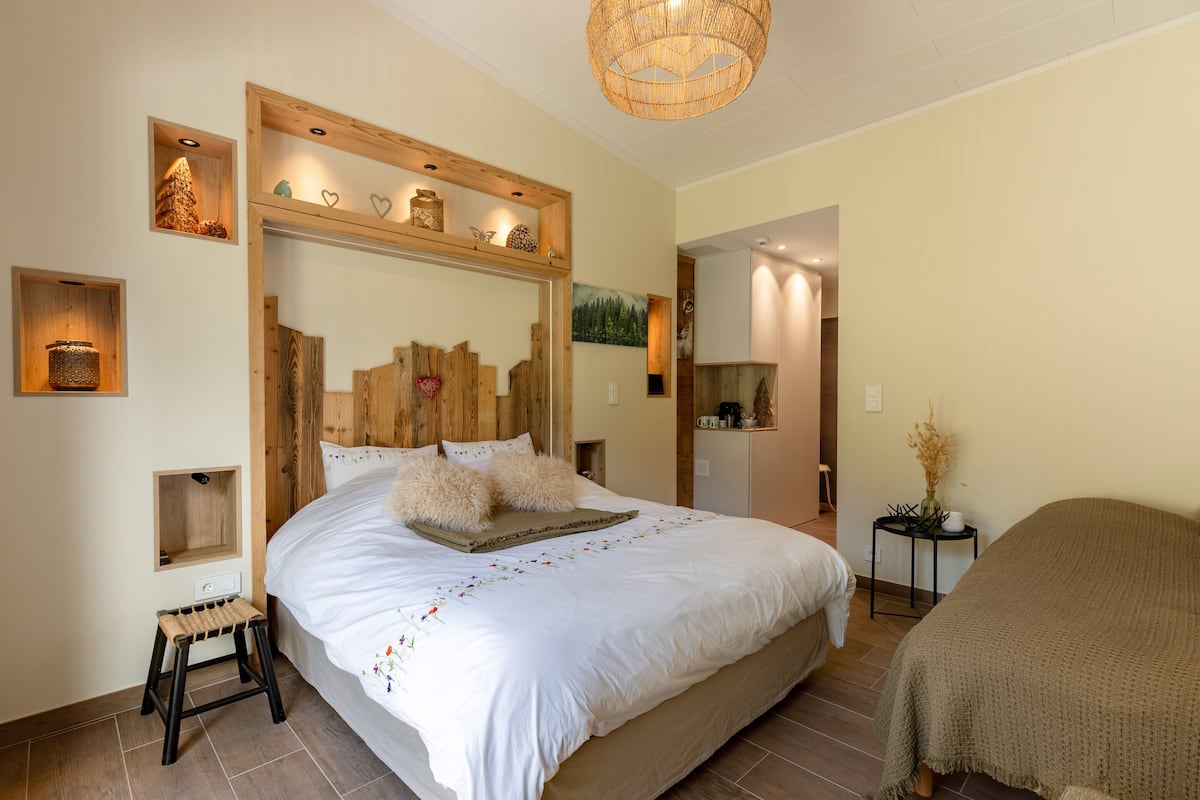 A bedroom with a large bed, wooden headboard, bedside tables, and a small stool.