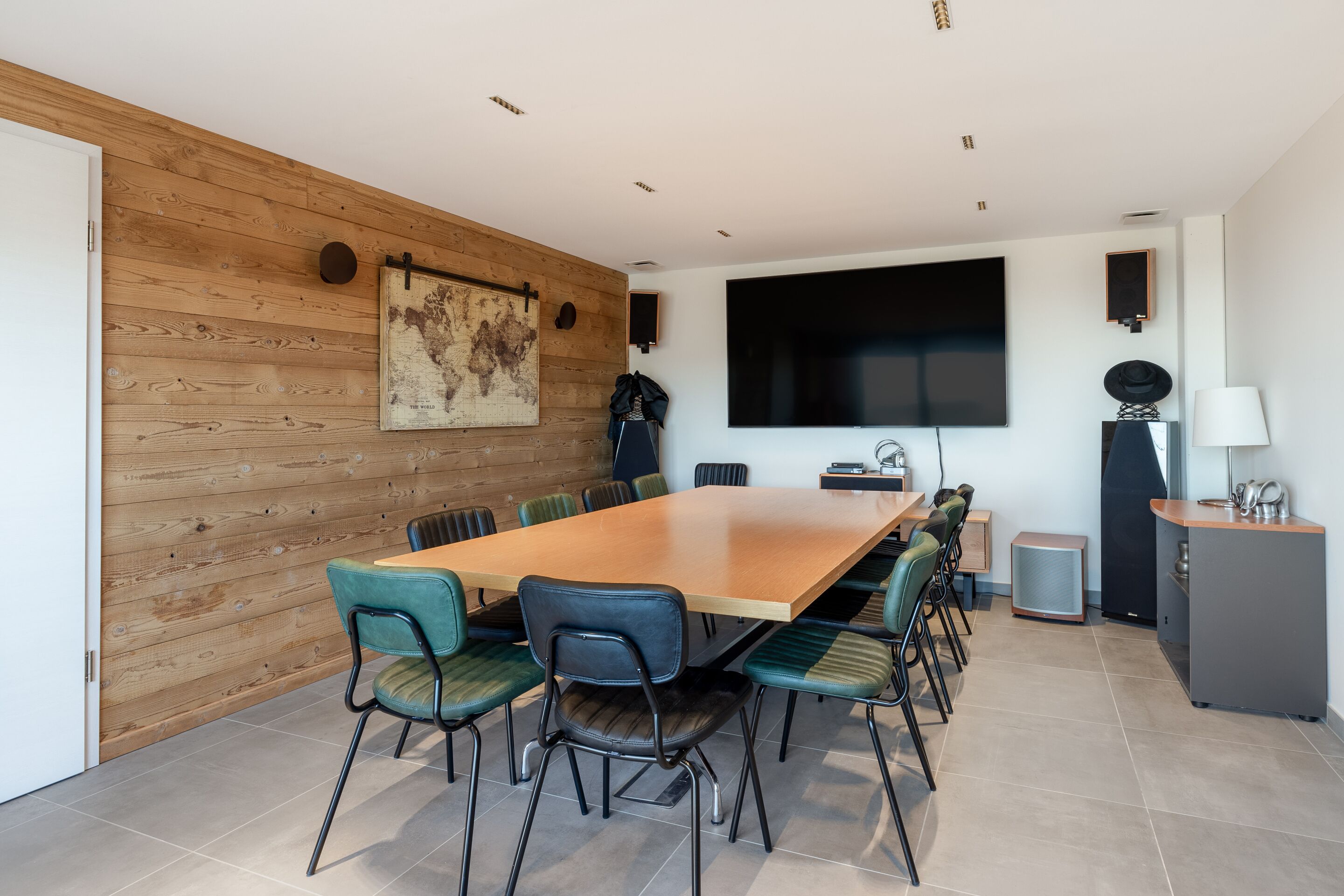 A conference room with a long table, chairs, a large TV, and a speaker.