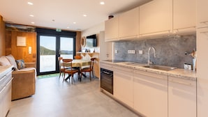Une cuisine moderne dotée d’un grand îlot central, d’un coin repas avec une table et des chaises, et d’un espace salon confortable avec un canapé et des coussins.