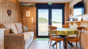 Une pièce chaleureuse avec un mur en bois, un canapé, une table à manger avec des chaises, un téléviseur à écran plat et une vue sur l’extérieur.