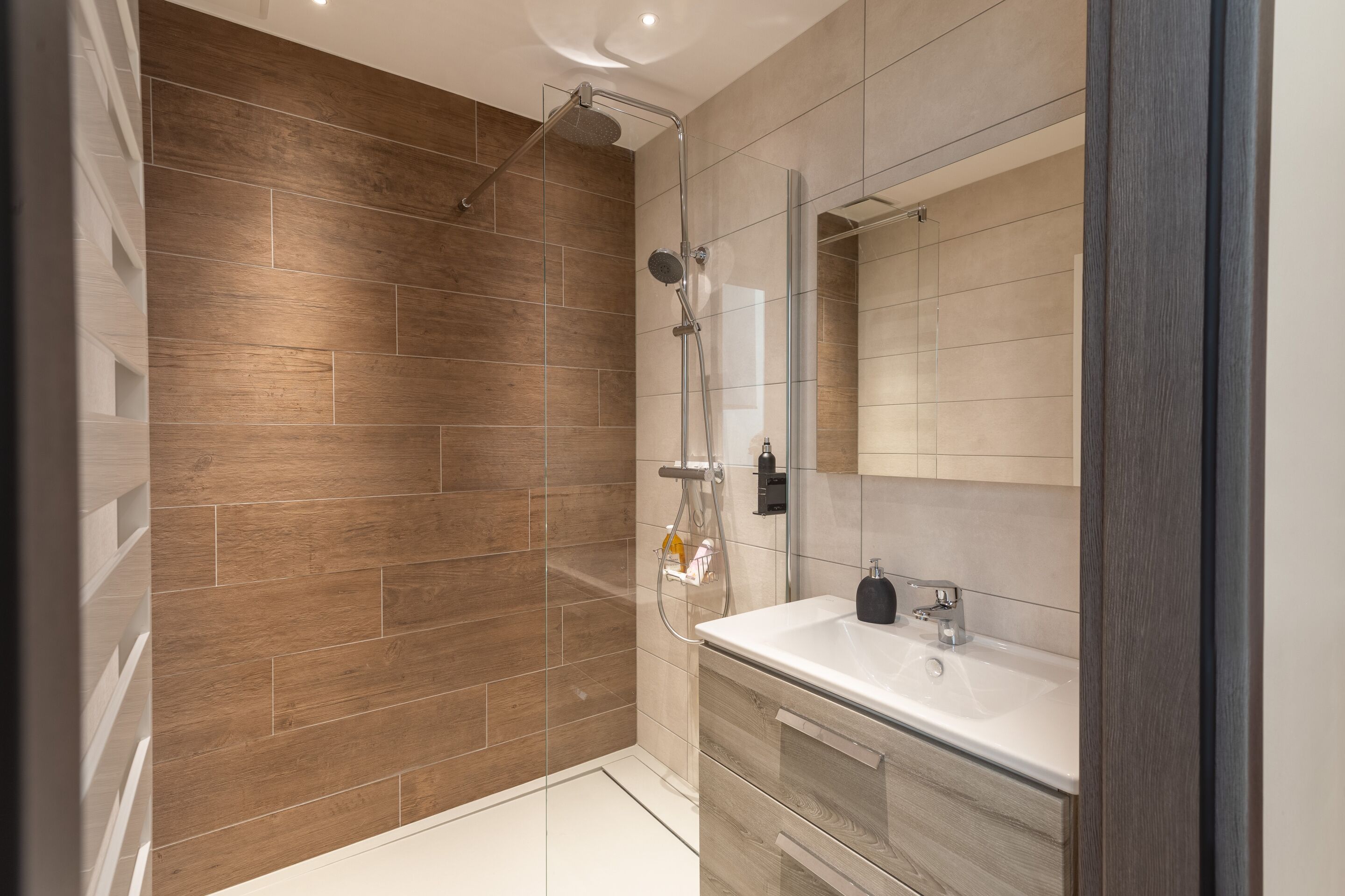 Ein modernes Badezimmer mit Holzwand in der Dusche, einer Glaskabine und einem Waschtisch mit Spiegel.