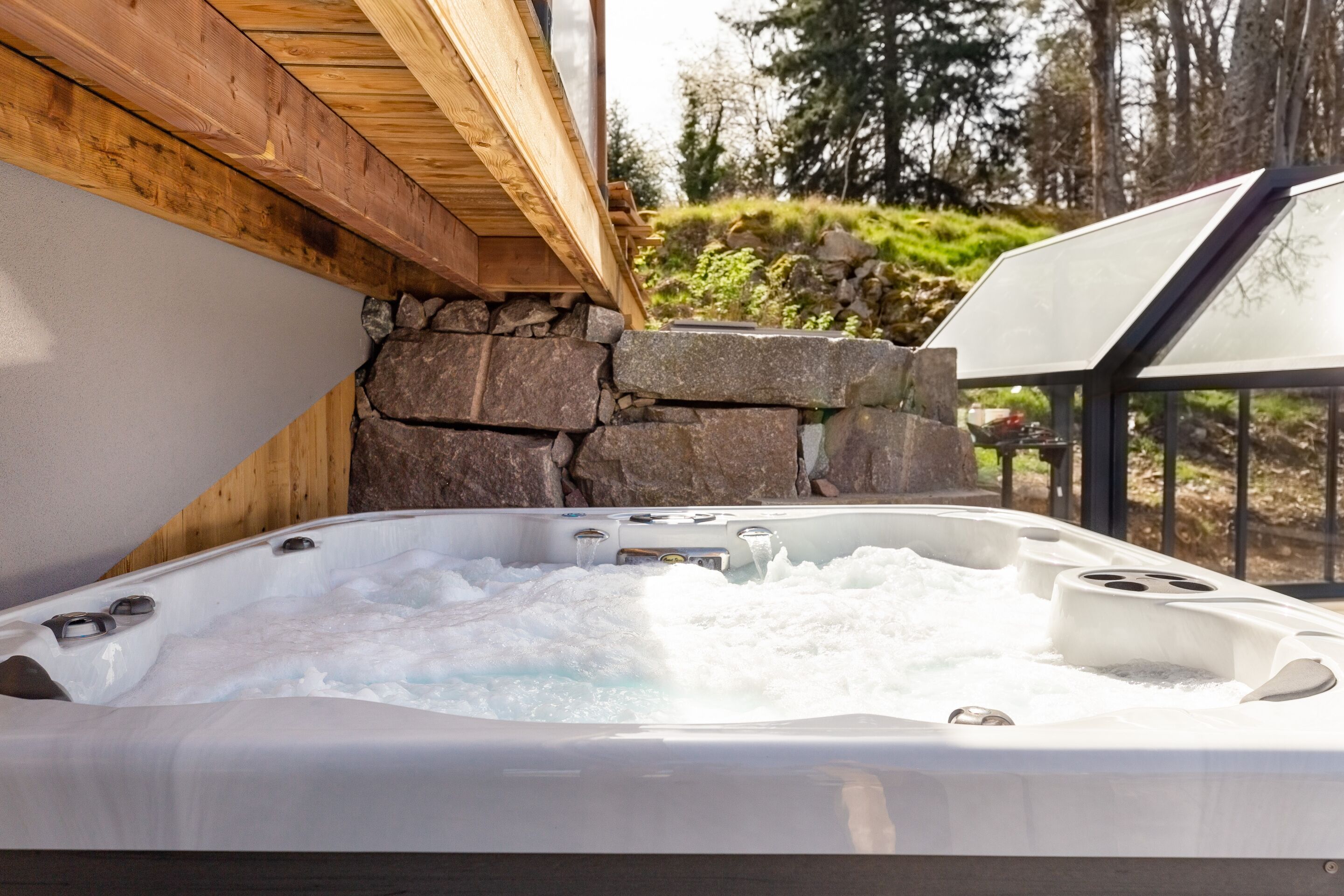 Ein Whirlpool mit Blick auf eine Steinwand, einer Holzbalkendecke und einer Glaseinfassung.