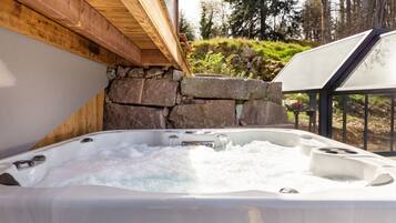 Ein Whirlpool mit Blick auf eine Steinwand, einer Holzbalkendecke und einer Glaseinfassung.