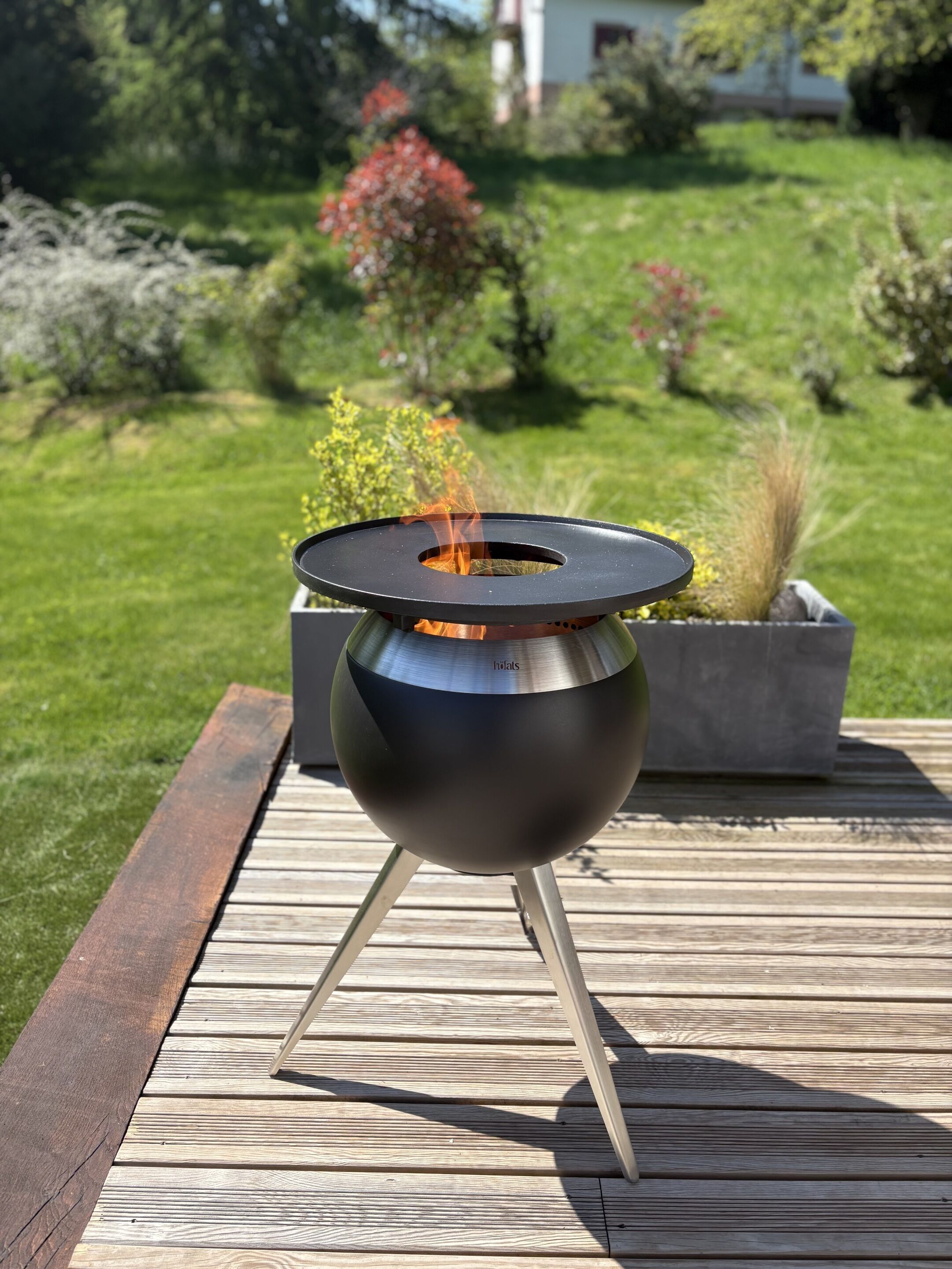 A portable outdoor grill with a round cooking surface and a chimney, placed on a wooden deck.