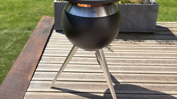 A portable outdoor grill with a round cooking surface and a chimney, placed on a wooden deck.
