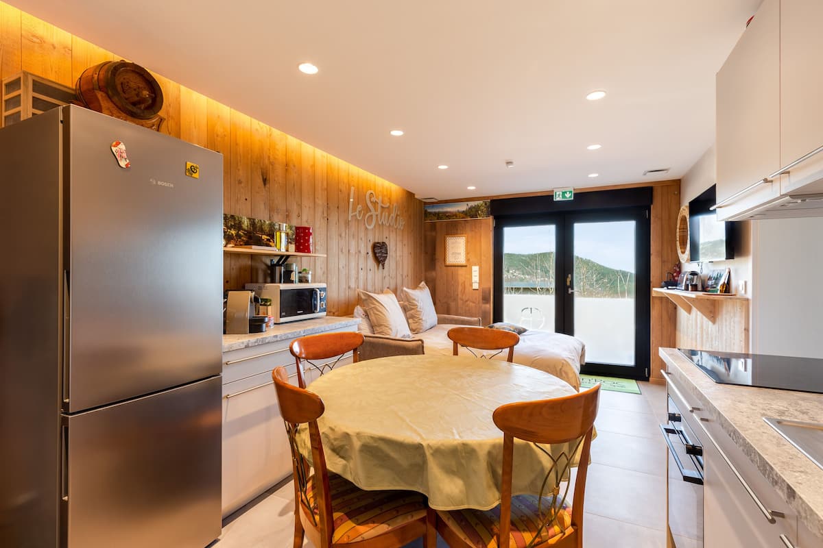 A modern kitchen with a Bosch refrigerator, wooden panel walls, a dining area with a table and chairs, and a view through a glass door.