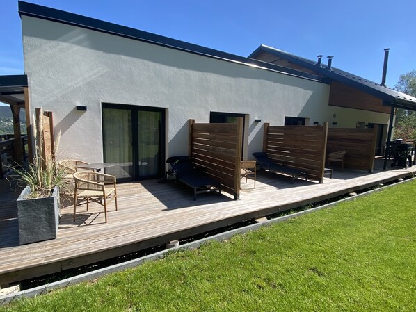 A modern building with a flat roof, large sliding glass doors, and a covered outdoor area with wooden furniture and a planter. - EDEN'ROC (Labaroche)