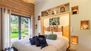 Une chambre avec un grand lit, une tête de lit en bois et une vue sur un jardin, accessible par une porte coulissante.