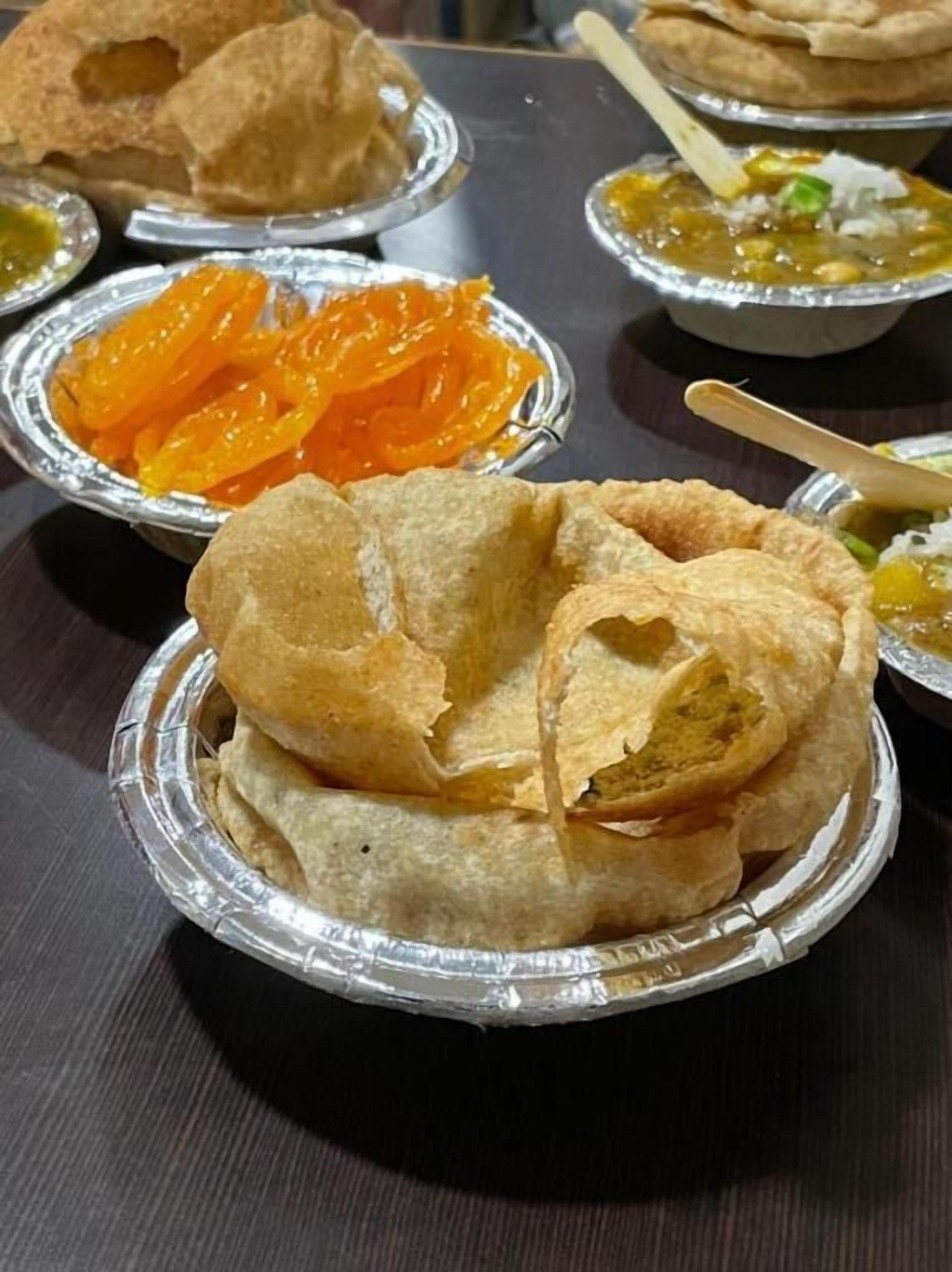 A table with various food items including fried snacks and a bowl of orange-colored sweets.