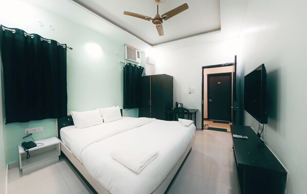 Habitación de hotel con cama, ventilador de techo, televisión, armario y escritorio con teléfono.