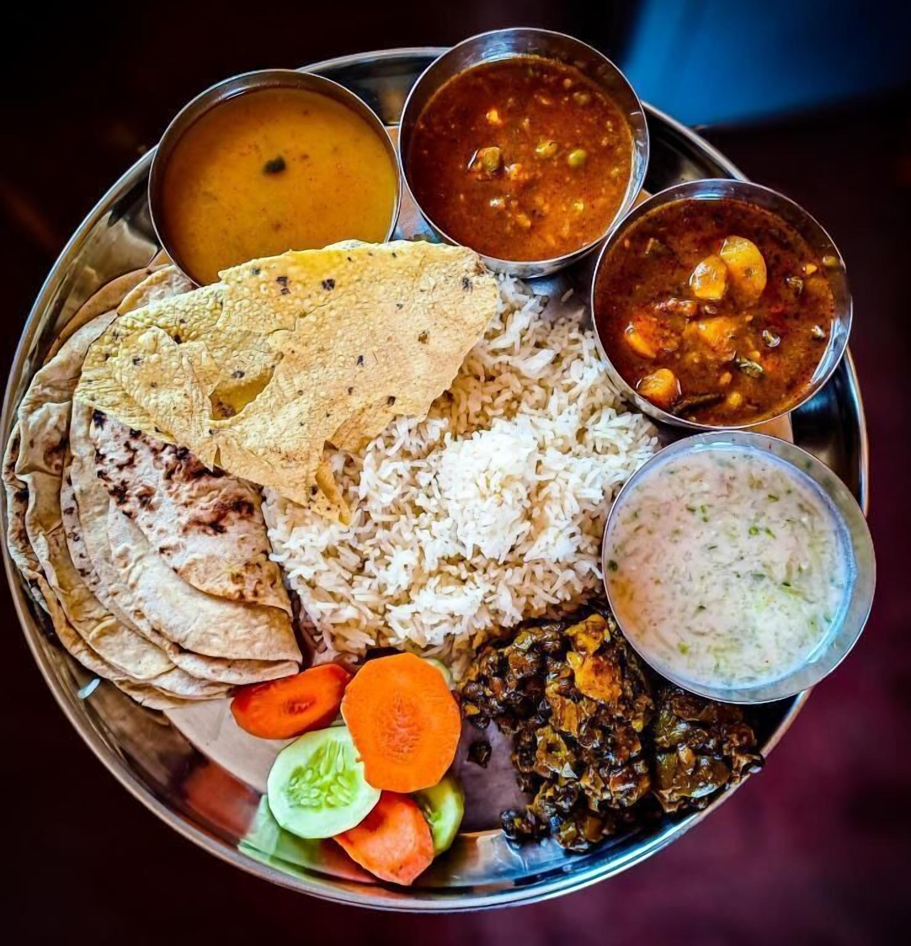 Una comida tradicional india con arroz, panes planos y varios curris sobre un plato de metal.