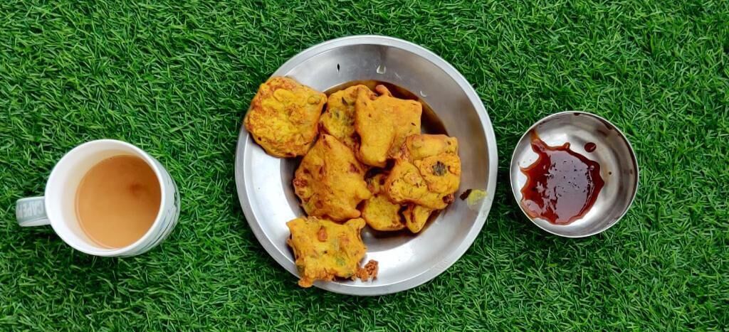 A metal plate with fried food, a small bowl of sauce, and a cup of tea on a green surface.
