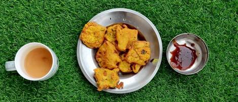 A metal plate with fried food, a small bowl of sauce, and a cup of tea on a green surface.