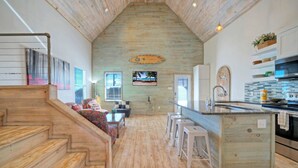 A spacious kitchen with wooden floors, a central island, bar stools, and a view of the beach through a window. - Shared Pool w/ Bay Views, Boat Dock | Fishing | Big Slough by AvantStay (Corpus Christi)