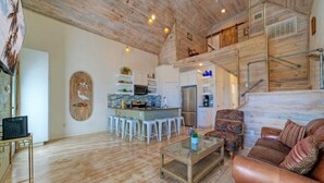 A spacious living area with a wooden floor, a sofa, a coffee table, and a kitchen in the background. - Shared Pool w/ Bay Views, Boat Dock | Fishing | Big Slough by AvantStay (Corpus Christi)