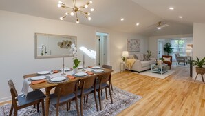 A spacious living area with a dining table set for six, a modern chandelier, and a cozy seating arrangement with a sofa and chairs. - Conch Cottage by AvantStay | Walk to Beach, Deck, Fireplace, Outdoor Dining (Isle Of Palms)