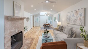 A spacious living room with a fireplace, a dining area, and a sofa. - Conch Cottage by AvantStay | Walk to Beach, Deck, Fireplace, Outdoor Dining (Isle Of Palms)