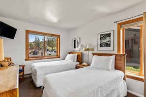 A hotel room with two beds, a television, a desk, and a window with a view of the street.