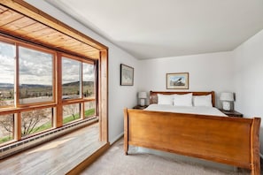 A bedroom with a wooden bed, two bedside tables, a window with a view of the countryside, and a framed picture on the wall.