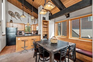 A modern kitchen with wooden beams, a large dining table, and a window overlooking a snowy landscape.