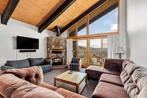 A living room with a stone fireplace, a flat-screen TV, and a large window with a balcony.