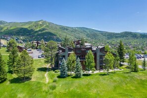 A multi-story hotel with a parking lot, surrounded by greenery and mountains.
