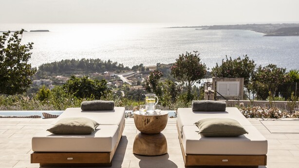 Een terras met twee ligbedden, een tafel met een glas, en uitzicht op zee.