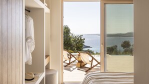 Een slaapkamer met een groot schuifglasraam dat leidt naar een balkon met uitzicht op zee.