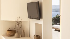 Een modern interieur met een flatscreen televisie aan de muur, een ingebouwde bank met decoratieve objecten, en een groot raam met uitzicht op het omliggende landschap.