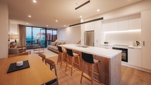 A modern kitchen with a central island, bar stools, and a dining area with a wooden table. - 95 Hardy Street Apartment 1 (Nelson)