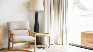 A room with a wooden chair, a small round table, a floor lamp, and a view through a window with curtains. - 95 Hardy Street Apartment 1 (Nelson)