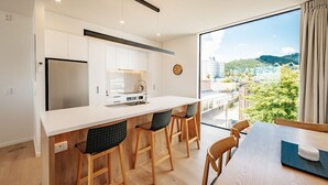 A modern kitchen with white cabinets, a stainless steel refrigerator, and a large window offering a view of a cityscape. - 95 Hardy Street Apartment 1 (Nelson)