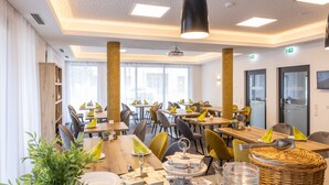 A modern dining area with multiple tables and chairs, a projector screen, and a large window providing natural light. - Haidinger Boutique Domizil (Oftering)