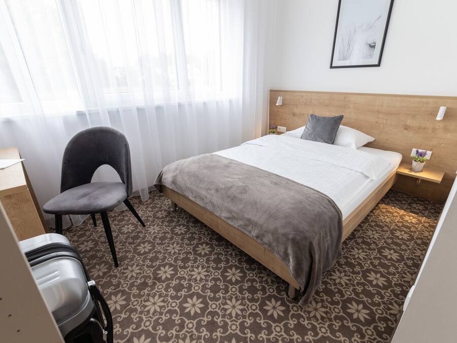 Ein Hotelzimmer mit Bett, Stuhl, Schreibtisch und einem Fenster mit Vorhängen.