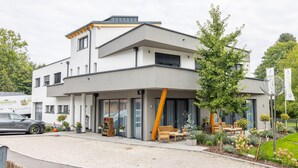 A modern two-story building with a covered outdoor seating area, a gravel driveway, and a parked delivery truck. - Haidinger Boutique Domizil (Oftering)