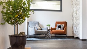A modern living room with two armchairs, a small side table, a potted plant, and a window with a view. - Haidinger Boutique Domizil (Oftering)